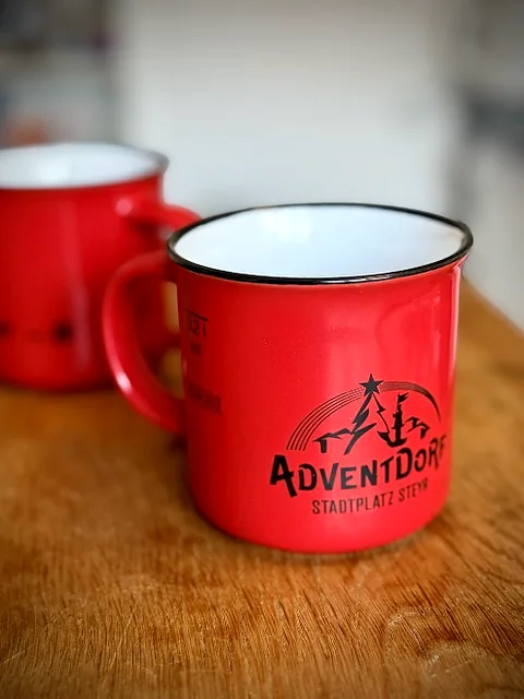 Rote Adventdorf-Tasse mit Logo auf einem Holztisch